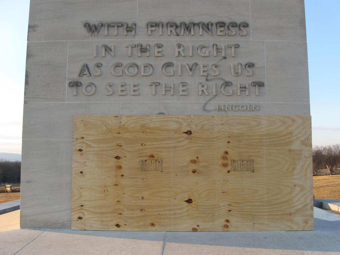 Large plywood covering vandalism on the Peace Light Memorial
